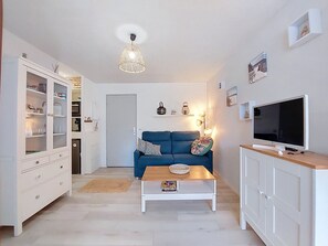 Ein Wohnzimmer mit blauem Sofa, Couchtisch, Fernseher, Schrank und einer Pendelleuchte.