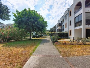 Ein Weg führt zu einem modernen Gebäude mit einem überdachten Gang, umgeben von Grünflächen und blauem Himmel.