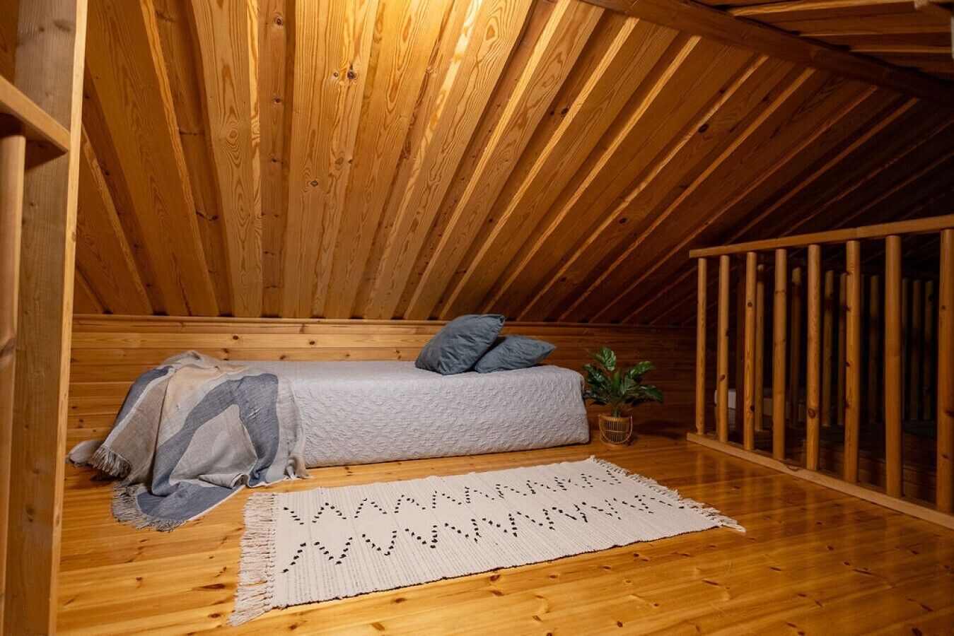 Un dormitorio tipo loft con techo de madera, una cama con almohadas, una planta y una alfombra tejida.