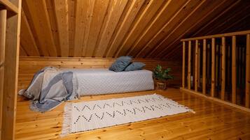Un dormitorio tipo loft con techo de madera, una cama con almohadas, una planta y una alfombra tejida.