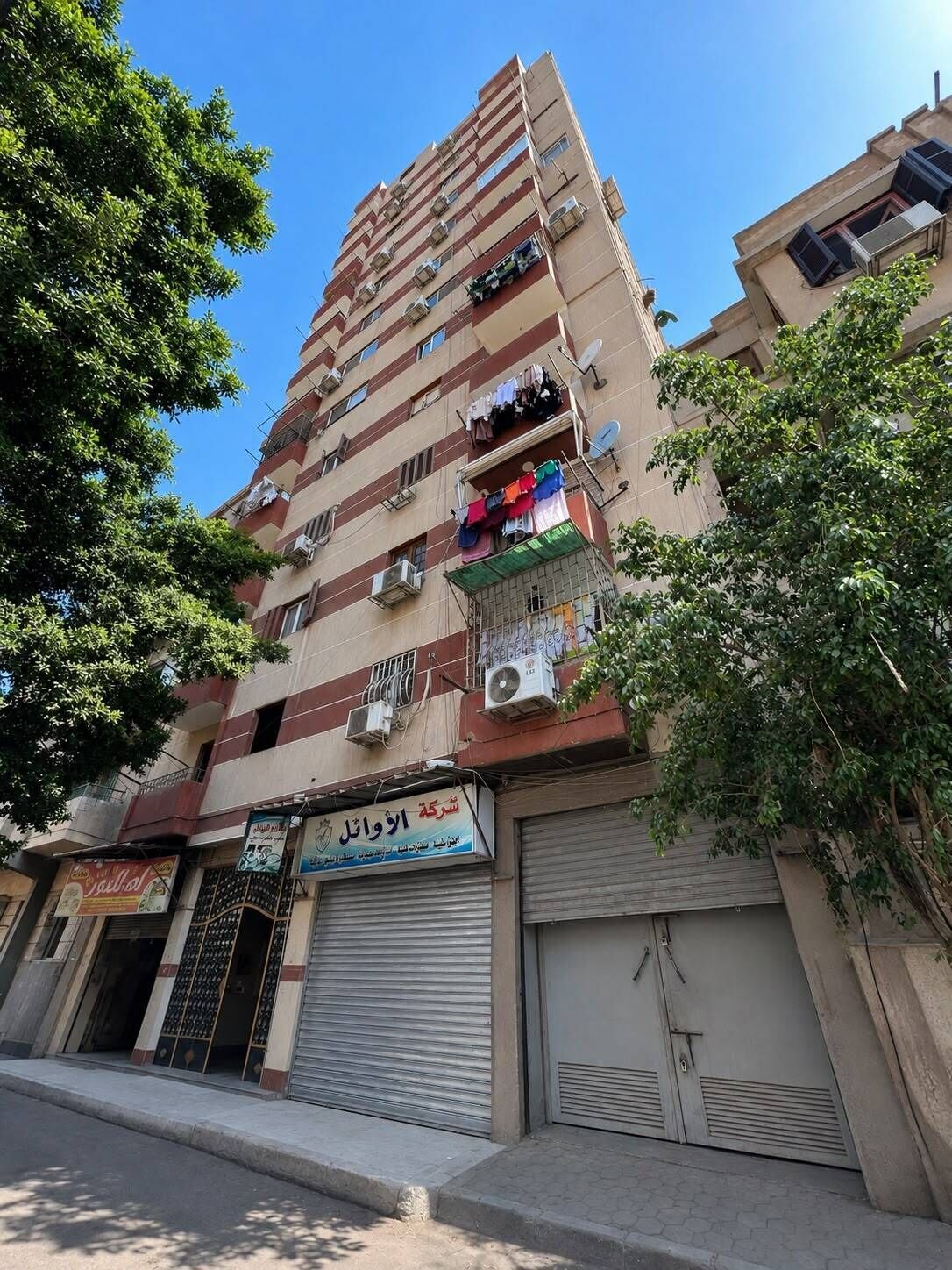 A multi-story residential building with balconies, air conditioning units, and a storefront with a closed shutter.
