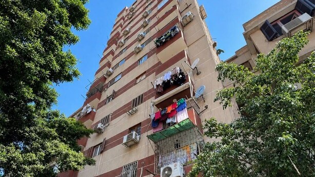 A multi-story residential building with balconies, air conditioning units, and a storefront with a closed shutter.
