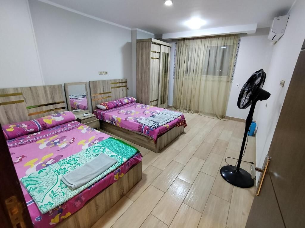 Habitación con dos camas, un armario, un ventilador y una ventana con cortinas.