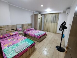 Una habitación con dos camas, un ventilador de pie y un armario.