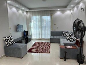 A modern living room with a grey sofa, ottoman, and a red and white patterned rug. - Comfy Luxurious Apartments East Cairo  (Cairo Governorate)