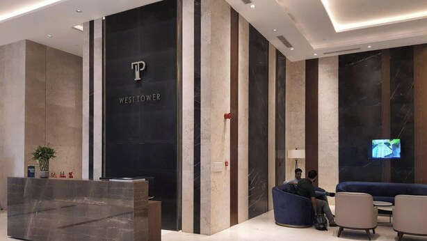 Ein moderner Empfangsbereich mit einer schwarzen Wand, die ein 'P'-Logo und den Schriftzug 'WEST TOWER' zeigt. Es gibt einen Empfangstresen, eine Sitzecke mit Sofas und einen an der Wand befestigten Bildschirm.