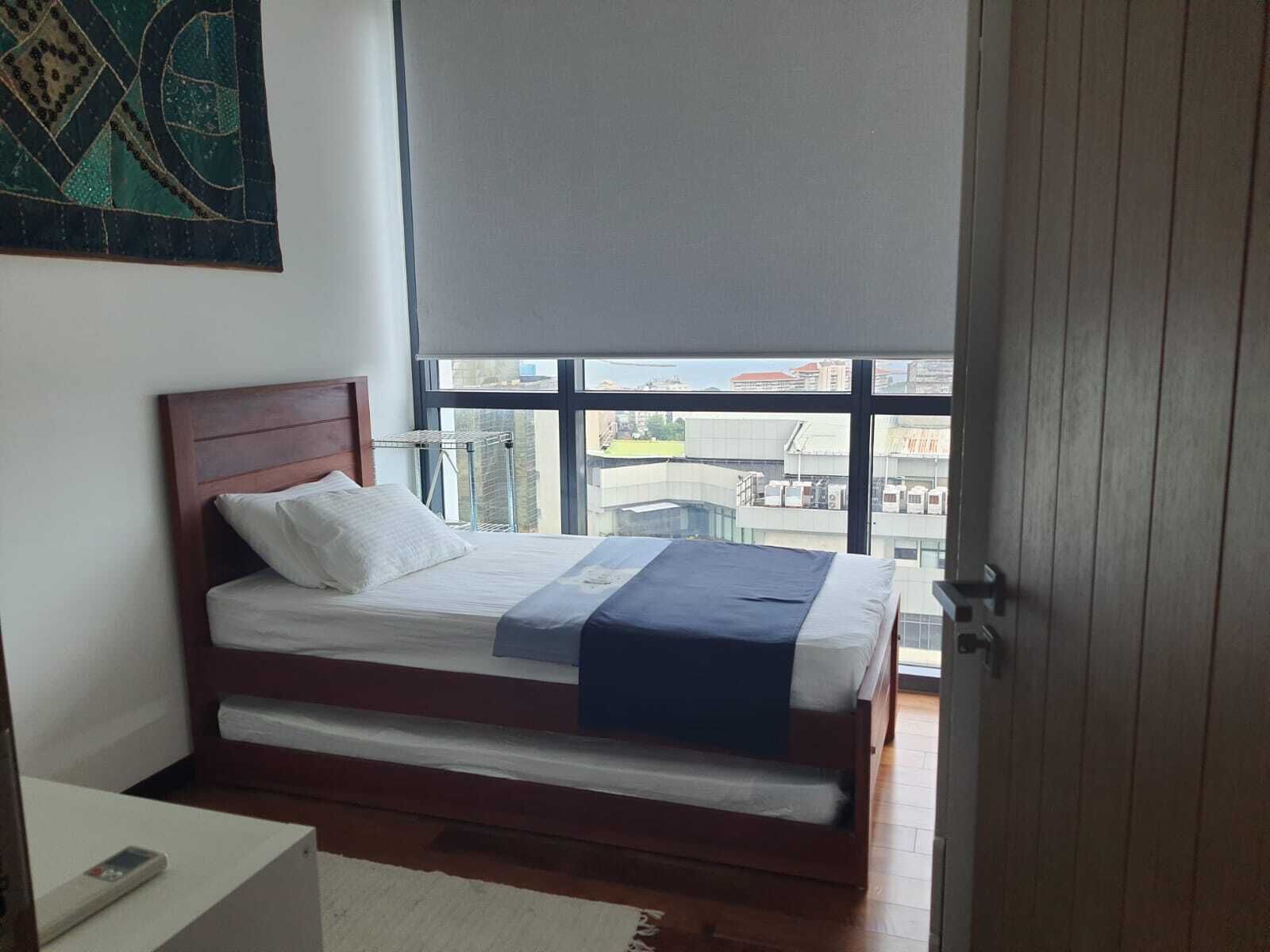 Quarto com cama, janela e vista para prédios.