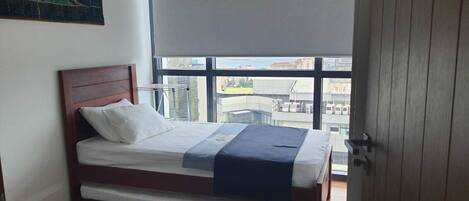 Quarto com cama, janela e vista para prédios.