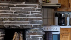 A stone fireplace with logs, a kitchen with wooden cabinets, a stove, and a coffee maker. - Varpunen - Peaceful 2BR Cabin in Ruka (Kuusamo)