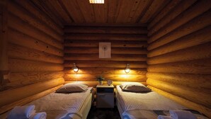 A log cabin room with two beds, each with a pillow and a rolled towel, a small table with a clock, and a framed picture on the wall. - Varpunen - Peaceful 2BR Cabin in Ruka (Kuusamo)