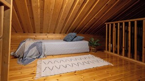 A cozy attic bedroom with a wooden ceiling, a single bed with pillows, a small plant, and a woven rug. - Varpunen - Peaceful 2BR Cabin in Ruka (Kuusamo)
