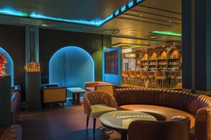 Un área de estar moderna con asientos de cuero, una barra con estantes llenos de botellas y una pared decorativa con líneas verticales.
