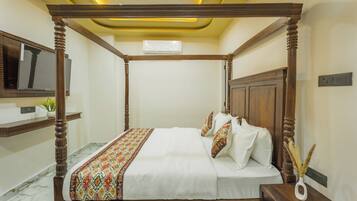 A four-poster bed with a patterned bedspread and pillows, a bedside table, a wall-mounted TV, and a marble floor.