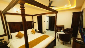 A four-poster bed with a wooden frame, a bedside table with a lamp, a chair, and a television. - Jigyasa palace hotel (Jaisalmer)