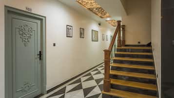 Ein Flur mit einem geometrisch gemusterten Boden, einer Treppe mit Holzsitzen und einem Handlauf sowie einer Tür mit einer Nummer.'
