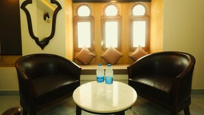 A room with two leather armchairs, a round table with two water bottles, and a window with three lights. - Jigyasa palace hotel (Jaisalmer)