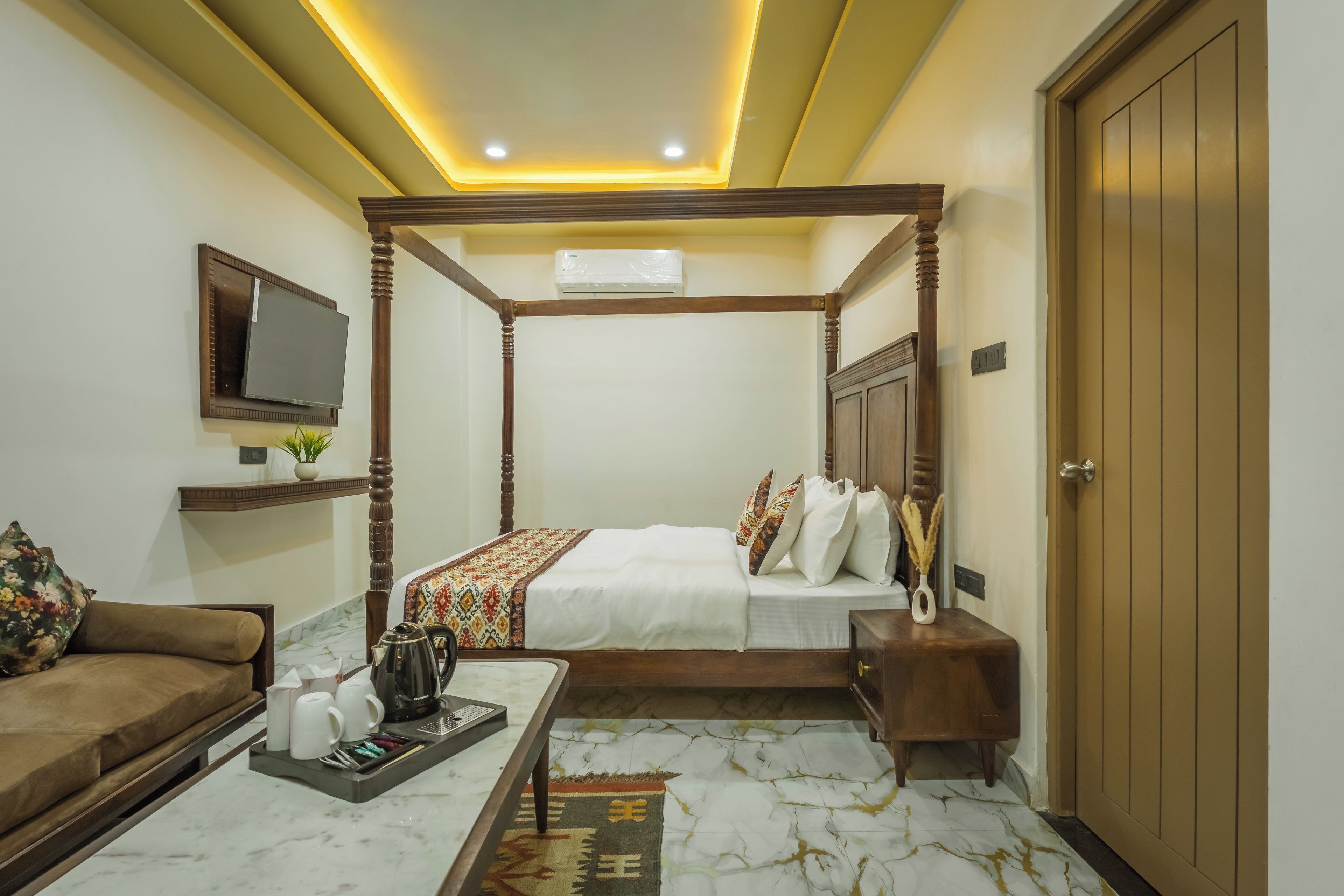 Quarto de hotel com cama de dossel, televisão na parede, sofá, mesa de centro com xícaras de chá e guarda-roupa de madeira.