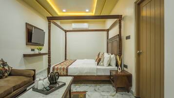 Quarto de hotel com cama de dossel, televisão na parede, sofá, mesa de centro com xícaras de chá e guarda-roupa de madeira.