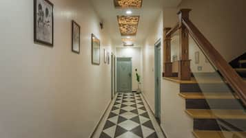A hallway with a checkered floor, framed pictures on the walls, and a staircase with wooden steps.