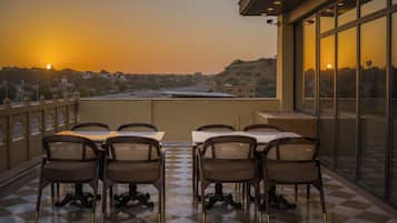 A terrace with tables and chairs, overlooking a cityscape during sunset.