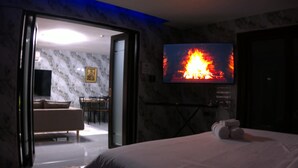 A hotel room with a bed, a television displaying a fire, a marble wall, and a door leading to a dining area. - Spacious fully self-contained 1-bedroom condo in Angeles City near Clark (Angeles)