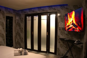 A hotel room with a bed, a television displaying a fire, and a sliding door.