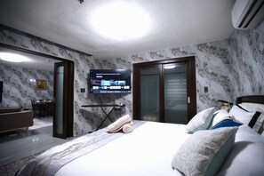 A hotel room with a bed, a TV mounted on the wall, a desk, and a chair. - Spacious fully self-contained 1-bedroom condo in Angeles City near Clark (Angeles)