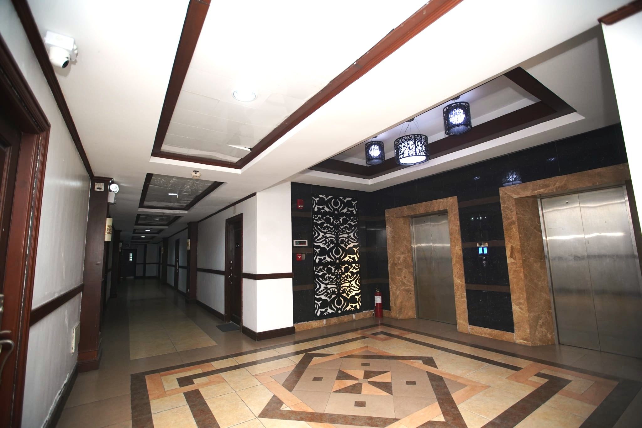 A hotel corridor with a patterned floor, a decorative wall panel, and two elevators.