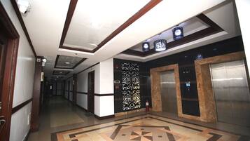 A hotel corridor with a patterned floor, a decorative wall panel, and two elevators.