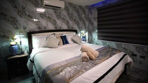 A hotel room with a marble-patterned wall, a bed with multiple pillows, a bedside lamp, and a window with blinds. - Spacious fully self-contained 1-bedroom condo in Angeles City near Clark (Angeles)