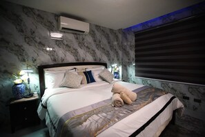 Habitación de hotel con pared de diseño de mármol, cama con muchas almohadas, lámpara de noche y ventana con persianas.
