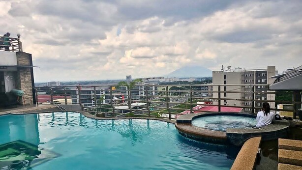 A rooftop pool with a view of buildings and a cloudy sky. - Spacious fully self-contained 1-bedroom condo in Angeles City near Clark (Angeles)
