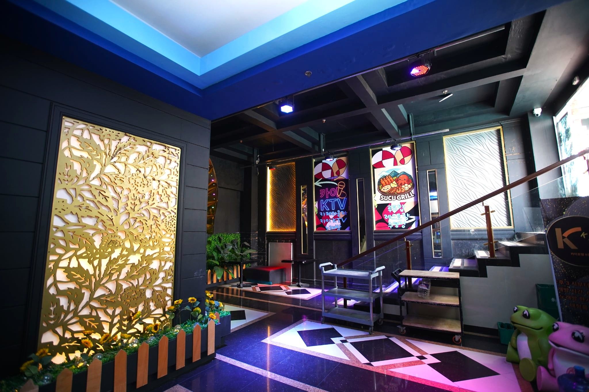 A modern interior with a reception desk, a staircase, and a neon sign advertising a grill.