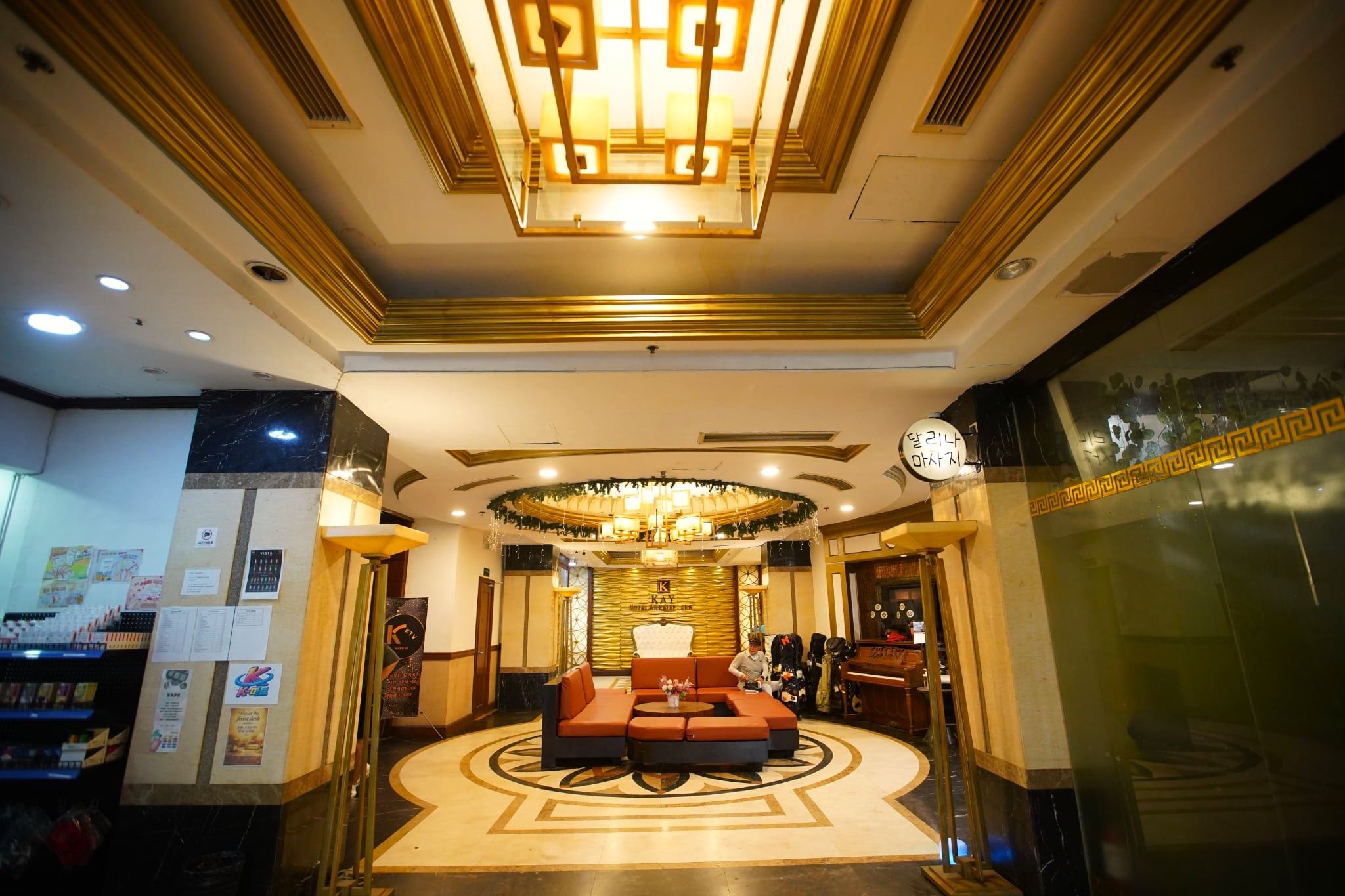 A hotel lobby with a central seating area, a chandelier, and a reception desk.