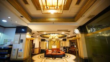 A hotel lobby with a central seating area, a chandelier, and a reception desk.