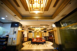 Un vestíbulo de hotel con un área de estar central, un candelabro y una mesa de recepción.
