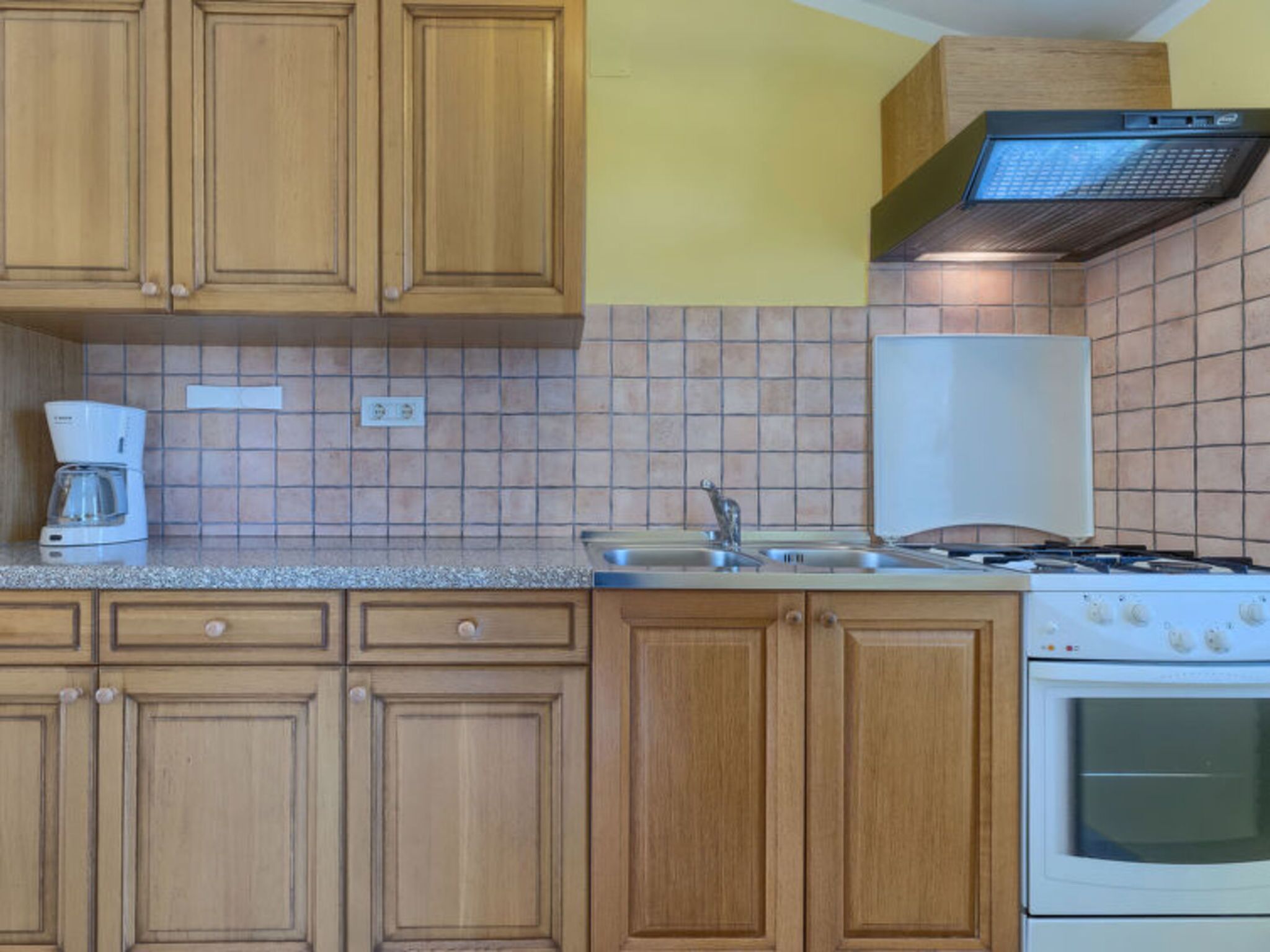 A kitchen with wooden cabinets, a stove, a coffee maker, and a tiled backsplash.
