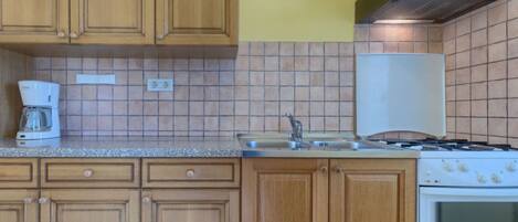 A kitchen with wooden cabinets, a stove, a coffee maker, and a tiled backsplash.