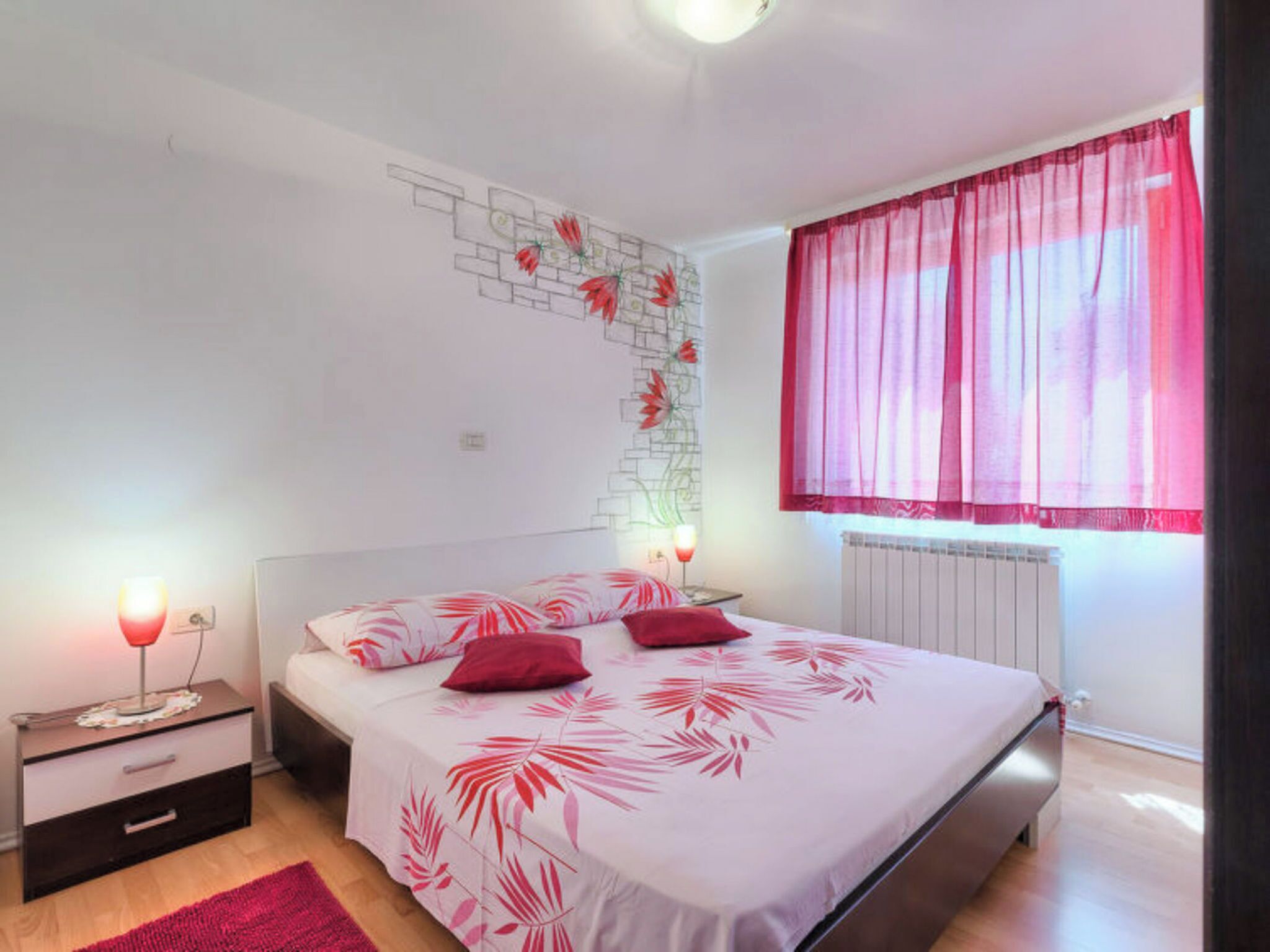 A bedroom with a bed, nightstands, a radiator, and a window with curtains.