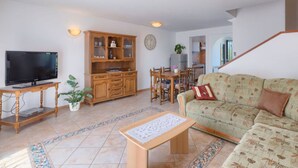 Una sala de estar con televisor, mueble de madera, mesa de comedor, sofá y una escalera.