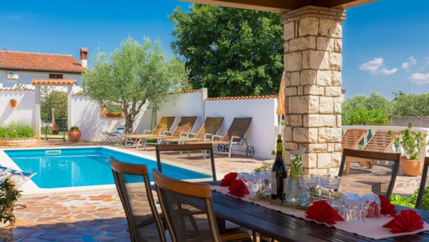 Zona de piscina con mesa lista para comer, sillas de descanso y un pilar de piedra.