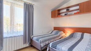 Un dormitorio con dos camas, una ventana con cortinas, un estante de madera sobre las camas y una alfombra pequeña en el suelo.