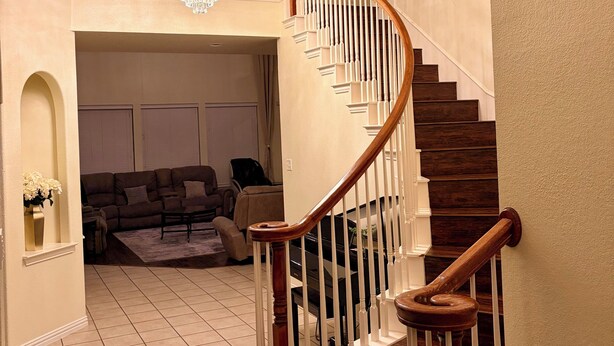 A staircase with wooden handrails and white balusters, leading to a second-floor landing with a chandelier. - Luxury Retreat Hot Tub, Office & Gym (Arlington)