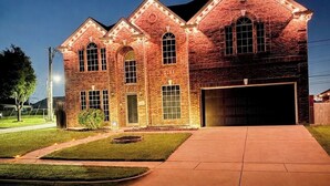 A brick building with a garage, a driveway, and a well-maintained lawn. - Luxury Retreat Hot Tub, Office & Gym (Arlington)