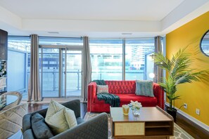 A modern living room with a red sofa, a coffee table, and a large window offering a view of buildings. - Aster Bay Hotel (Toronto)