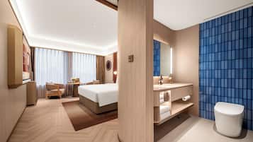 Quarto de hotel com cama, mesa de cabeceira, abajur e vista para a paisagem urbana.