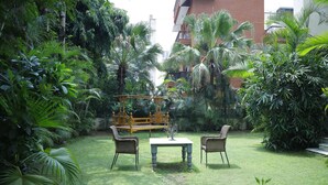 A lush garden with a wooden play structure, two wicker chairs, and a small table.