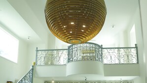A spacious living area with a high ceiling, a large wooden chandelier, a staircase with ornate railings, and a view of the outdoors through large windows.