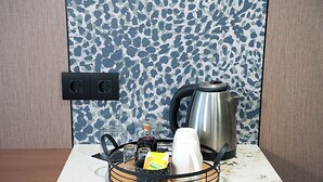 A kitchen counter with a kettle, a coffee maker, and a bottle of pickles.