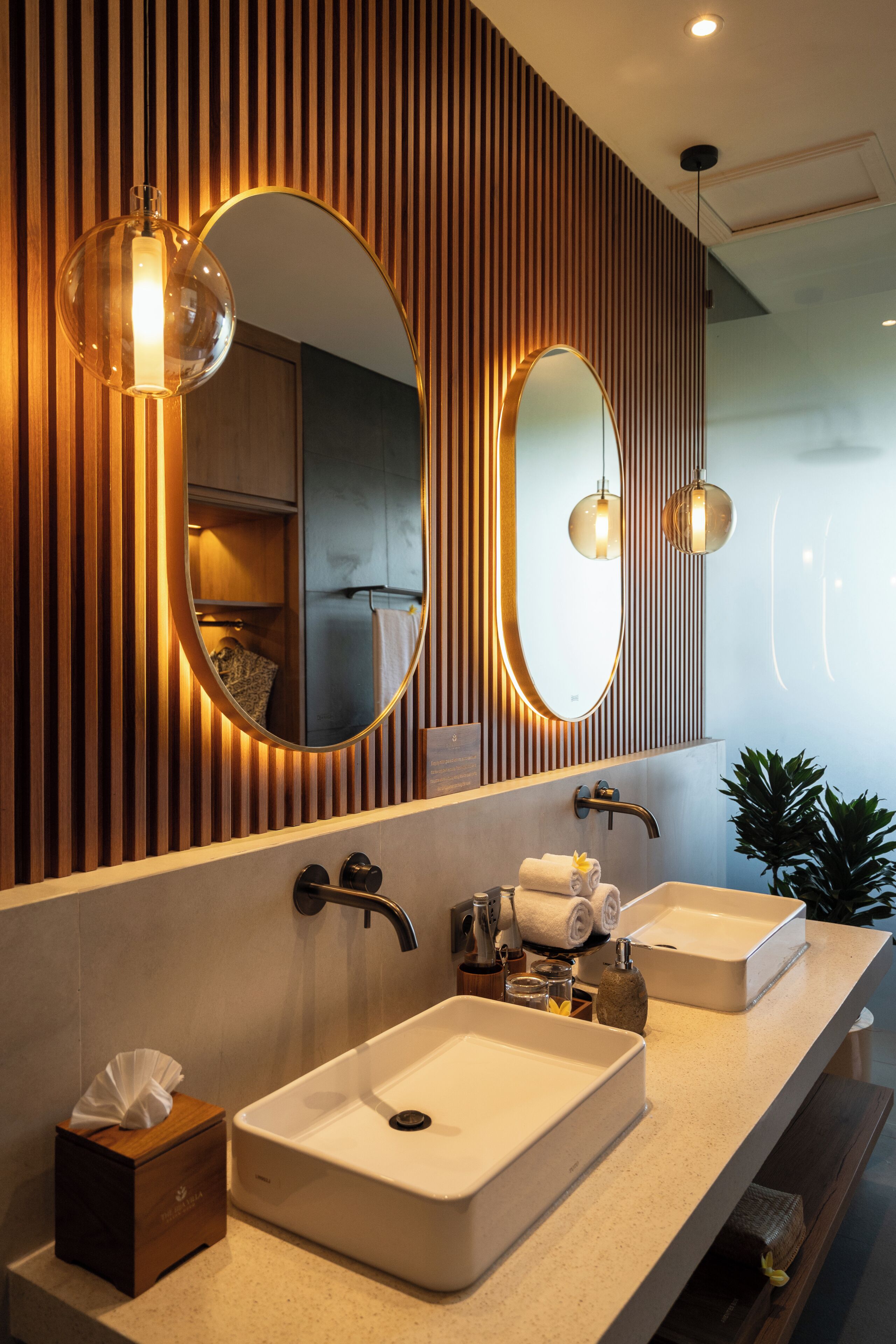 A modern bathroom with two sinks, wooden paneling, and pendant lighting.